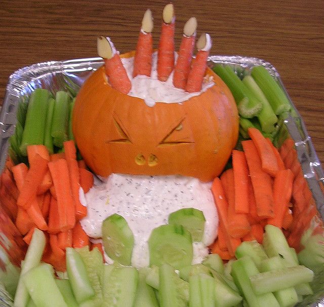 A photo of a veggie tray where in the middle, a pumpkin is carved so it looks like it is vomiting ranch dressing.